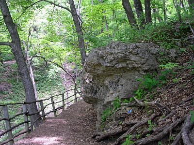 [A wooden split-rail fence marks the edge of the ledge with a trail to its right. There is a large rock hillside on the right.]